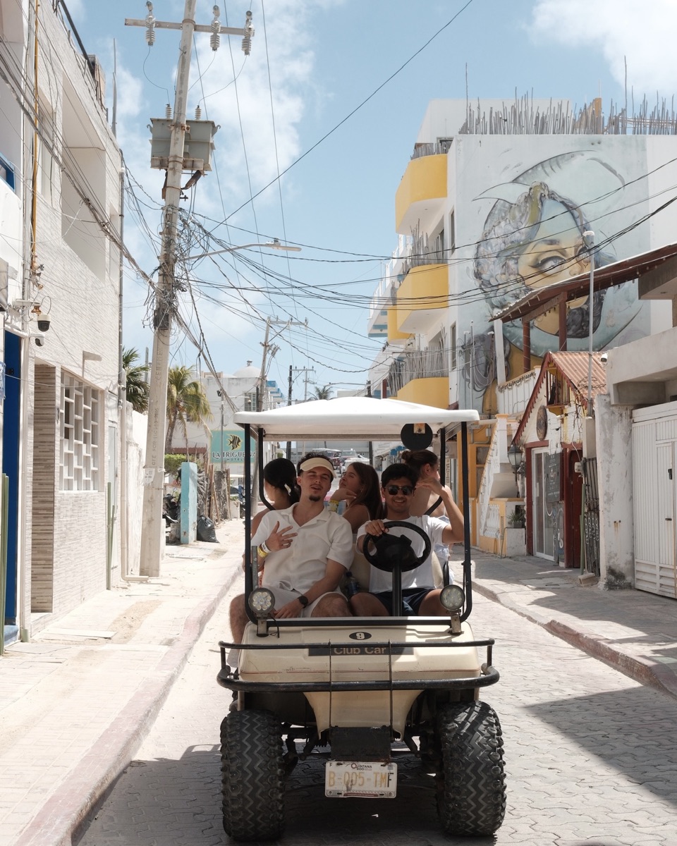 Friends riding a golf cart along a sunny street in Cancun